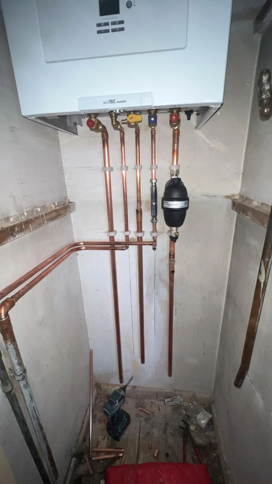 A Vaillant ecoTEC boiler in a cupboard with new clipped copper pipework and a magnetic filter below it
